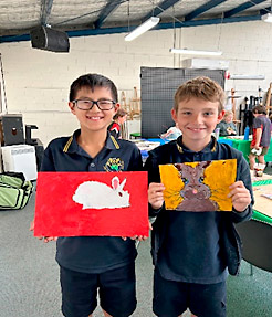 Upstart for Kids class age 7-11. Image of two boys holding their artwork of rabbits painted on brightly coloured backgrounds.