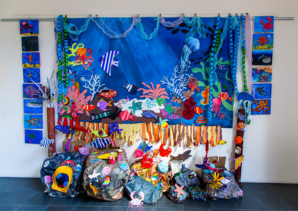 Under the Sea by the Upstart Kids. A children's art installationt featuring brightly coloured paintings and models of sea creatures against an undersea painted backdrop and 3D modeled rocks.