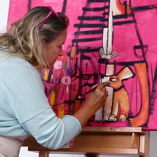 Artist Janine Daddo demonstrating her painting techniques - painting a quirky dog character on a canvas with hot pink background.