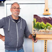 Ben Winspear with completed demo painting of a landscape with rocky hill and trees in foreground.