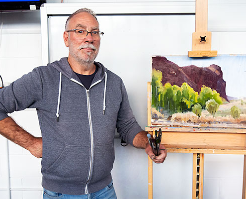 Ben Winspear with completed demo painting of a landscape with rocky hill and trees in foreground.