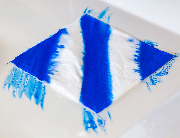 Geometric patterns - first colour. Blue diagonal stripes painted across a square of white fabric.